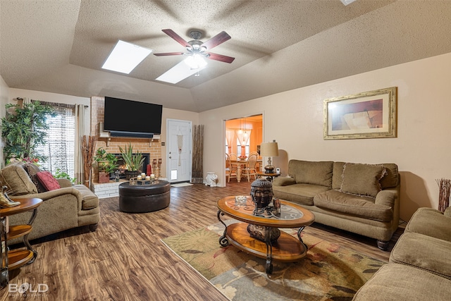 living room featuring vaulted ceiling with skylight, wood-type flooring, a textured ceiling, a brick fireplace, and ceiling fan