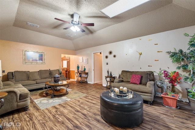 living room featuring ceiling fan, a textured ceiling, vaulted ceiling with skylight, and wood-type flooring