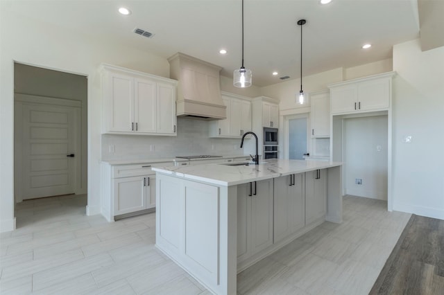 kitchen with white cabinetry, sink, and an island with sink