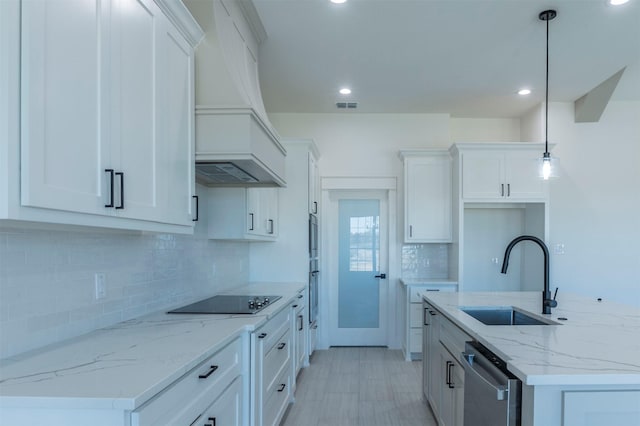 kitchen with black electric stovetop, custom exhaust hood, sink, white cabinets, and hanging light fixtures