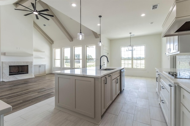 kitchen with a high end fireplace, sink, decorative light fixtures, light hardwood / wood-style flooring, and an island with sink