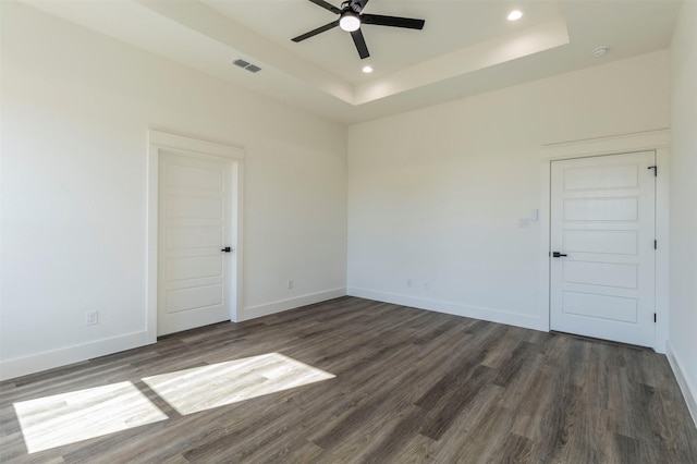 spare room with ceiling fan, dark hardwood / wood-style flooring, and a tray ceiling