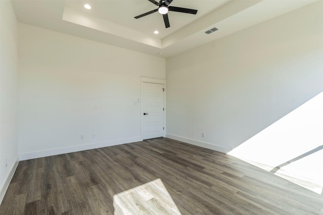 unfurnished room featuring a tray ceiling, ceiling fan, and dark hardwood / wood-style flooring