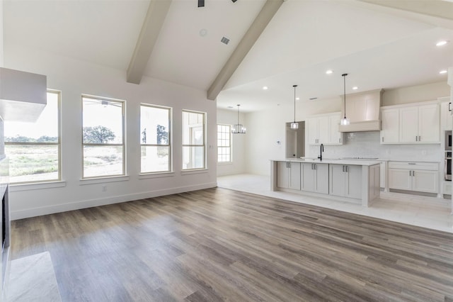 unfurnished living room featuring beam ceiling, high vaulted ceiling, light hardwood / wood-style floors, and ceiling fan with notable chandelier