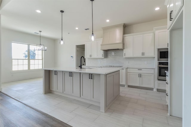 kitchen featuring premium range hood, sink, oven, and a center island with sink