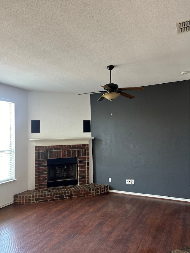 unfurnished living room featuring a textured ceiling, dark hardwood / wood-style floors, ceiling fan, and a brick fireplace