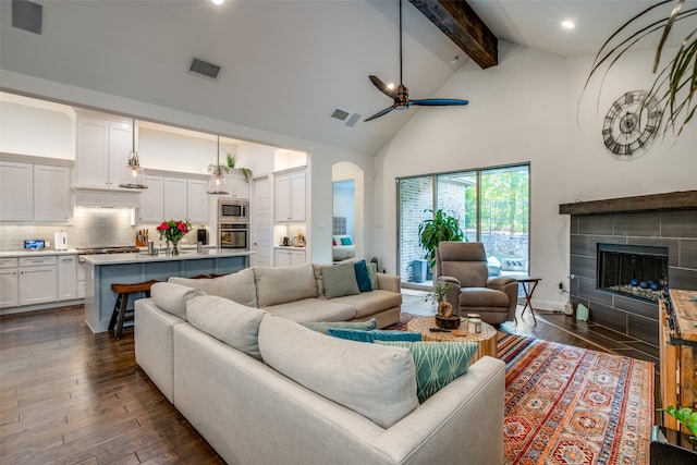 living room with beamed ceiling, dark hardwood / wood-style floors, a tiled fireplace, high vaulted ceiling, and ceiling fan