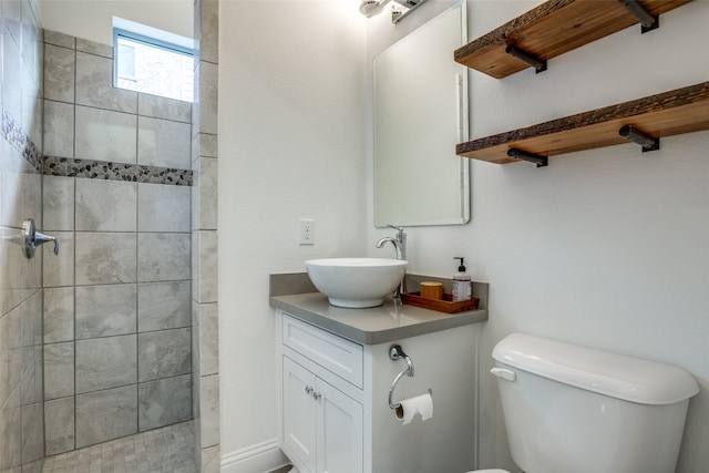 bathroom featuring a tile shower, vanity, and toilet