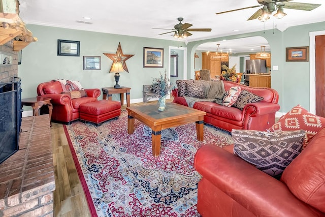 living room featuring ceiling fan with notable chandelier, wood-type flooring, a fireplace, and ornamental molding