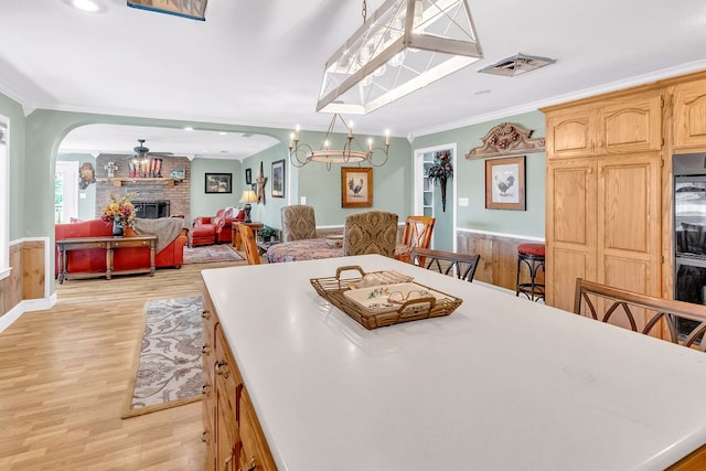 kitchen featuring hanging light fixtures, a brick fireplace, a breakfast bar, crown molding, and light hardwood / wood-style floors