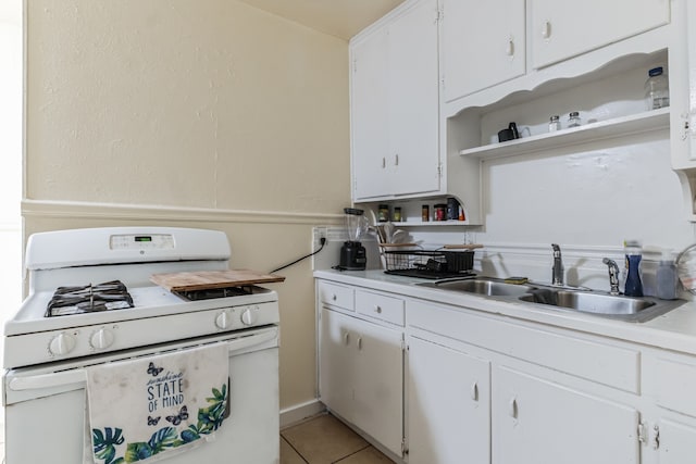 kitchen with white range with gas stovetop, light tile patterned flooring, sink, and white cabinets