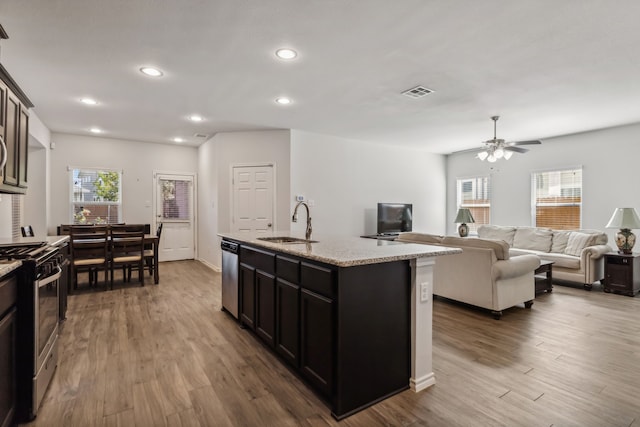 kitchen with ceiling fan, an island with sink, sink, stainless steel appliances, and hardwood / wood-style floors