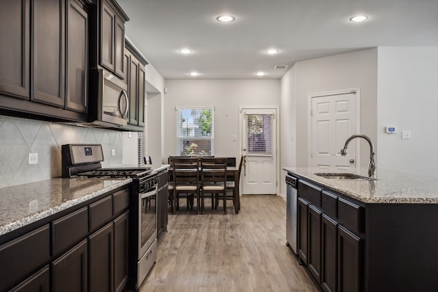 kitchen with a kitchen island with sink, sink, light hardwood / wood-style flooring, stainless steel appliances, and light stone countertops