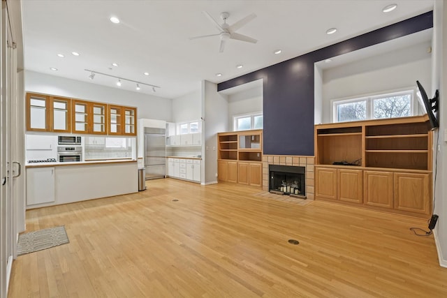 unfurnished living room with ceiling fan, a healthy amount of sunlight, a fireplace, and light hardwood / wood-style flooring