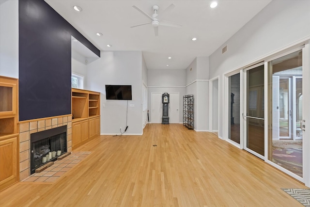 unfurnished living room with a tiled fireplace, light hardwood / wood-style floors, and ceiling fan