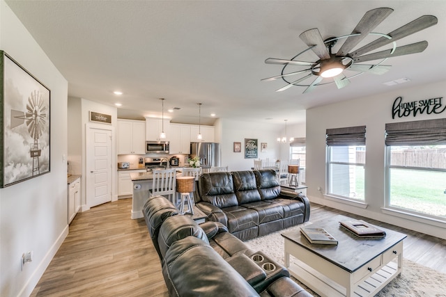 living room featuring ceiling fan with notable chandelier and light hardwood / wood-style floors