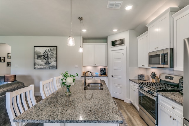 kitchen with light hardwood / wood-style floors, a kitchen island with sink, sink, hanging light fixtures, and appliances with stainless steel finishes