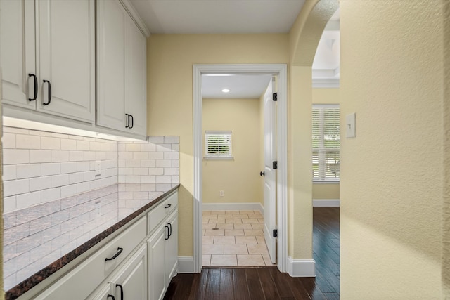 kitchen with decorative backsplash, dark stone countertops, white cabinetry, and dark hardwood / wood-style floors