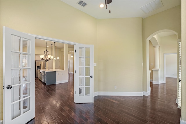 unfurnished room with french doors, an inviting chandelier, a towering ceiling, and dark wood-type flooring