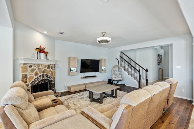 living room with a stone fireplace and dark wood-type flooring