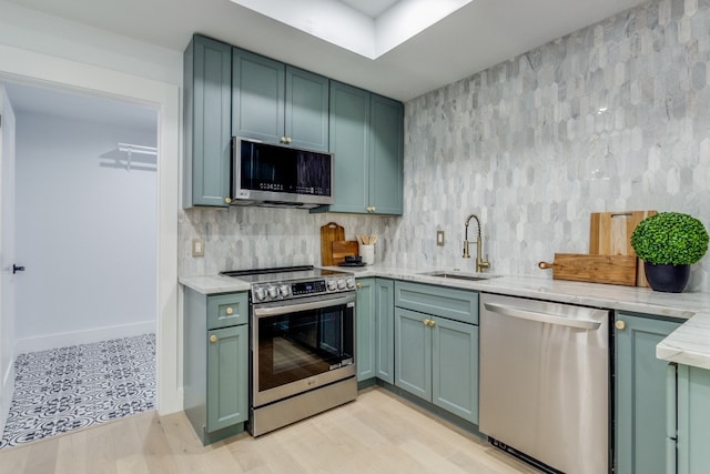 kitchen with green cabinetry, stainless steel appliances, light wood-type flooring, and sink