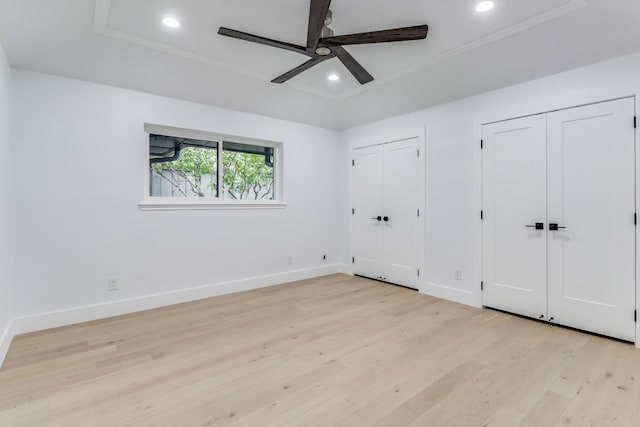 unfurnished bedroom with light wood-type flooring, ceiling fan, and multiple closets