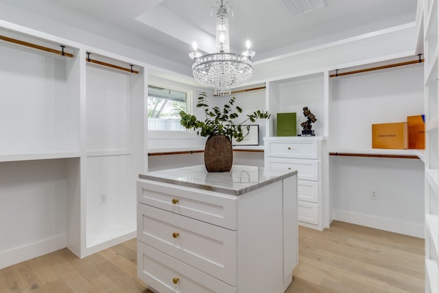 walk in closet with built in desk, a chandelier, light hardwood / wood-style floors, and a raised ceiling