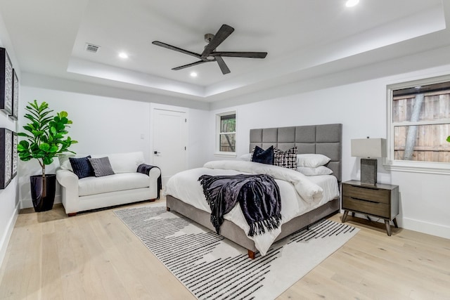 bedroom featuring ceiling fan, light hardwood / wood-style flooring, and a tray ceiling