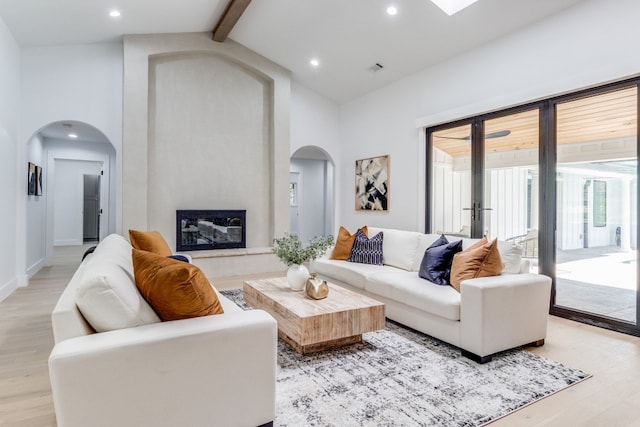 living room with high vaulted ceiling, beam ceiling, a high end fireplace, and light hardwood / wood-style flooring