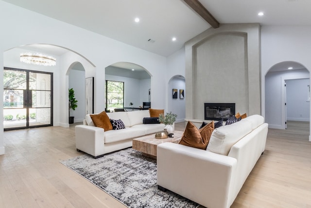 living room featuring light wood-type flooring, a fireplace, beam ceiling, and a wealth of natural light