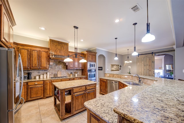 kitchen featuring a barn door, a kitchen island, stainless steel appliances, decorative light fixtures, and sink