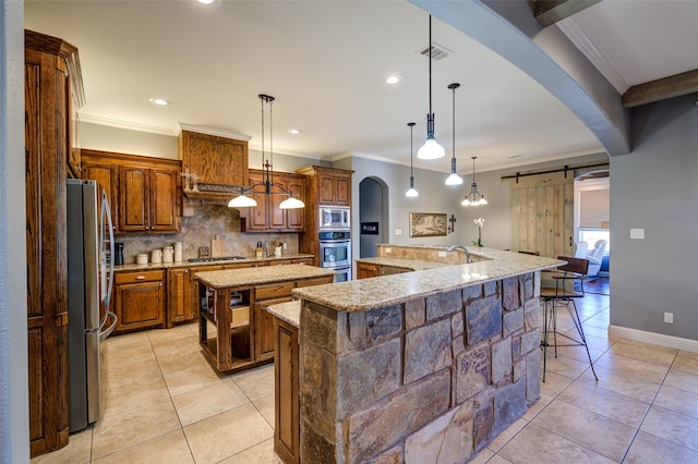 kitchen with decorative light fixtures, a large island with sink, appliances with stainless steel finishes, a barn door, and decorative backsplash