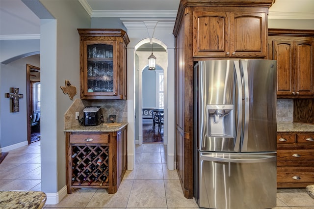 kitchen with stainless steel fridge, light tile patterned flooring, tasteful backsplash, light stone countertops, and ornamental molding