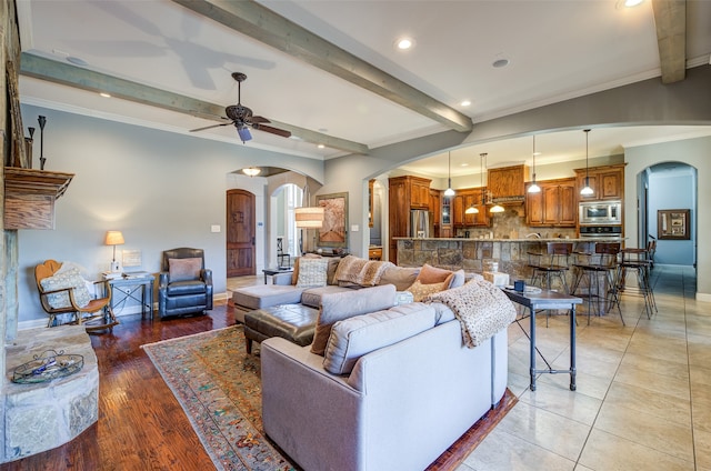 living room with beamed ceiling, ornamental molding, ceiling fan, and light hardwood / wood-style flooring