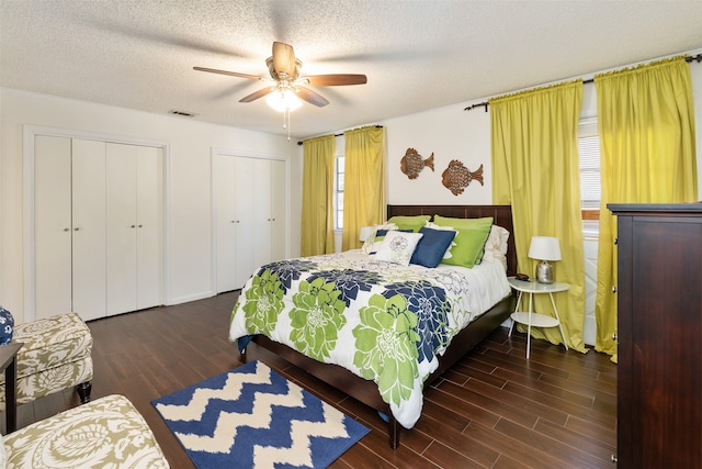 bedroom with two closets, ceiling fan, dark wood-type flooring, and a textured ceiling