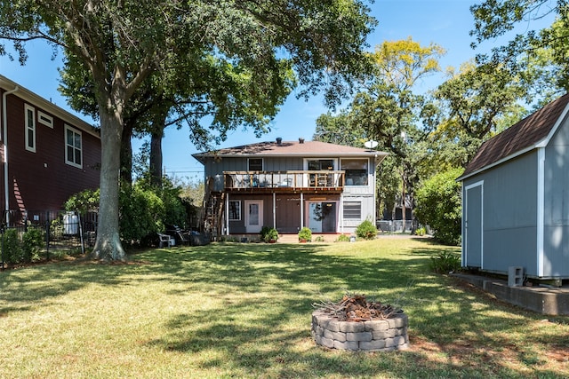 back of property featuring a fire pit, a wooden deck, a yard, and a shed