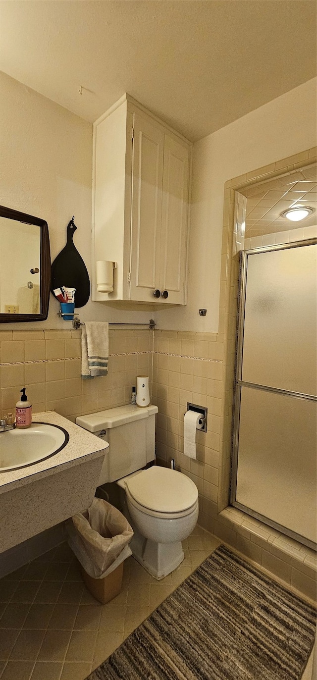 bathroom with tile walls, tile patterned flooring, sink, a shower with door, and toilet