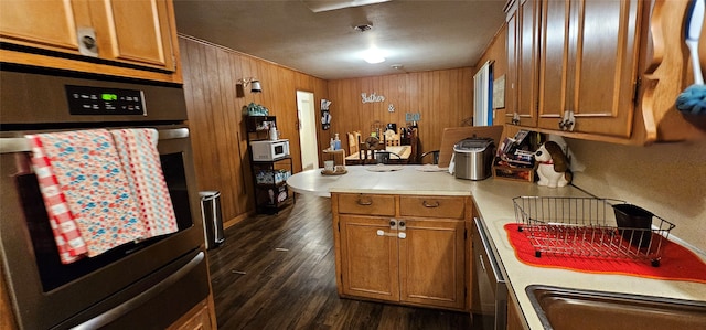 kitchen with wooden walls, appliances with stainless steel finishes, sink, and dark hardwood / wood-style flooring