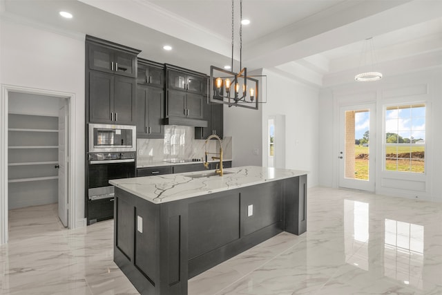 kitchen featuring appliances with stainless steel finishes, hanging light fixtures, decorative backsplash, an island with sink, and light stone countertops