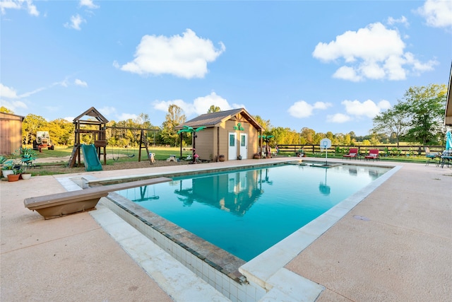 view of pool with a playground, an outdoor structure, and a diving board