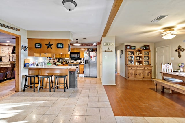 kitchen featuring ceiling fan, kitchen peninsula, appliances with stainless steel finishes, a kitchen breakfast bar, and light hardwood / wood-style floors