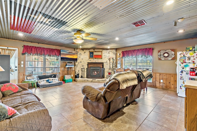 living room featuring wooden walls, tile patterned flooring, ceiling fan, and a stone fireplace