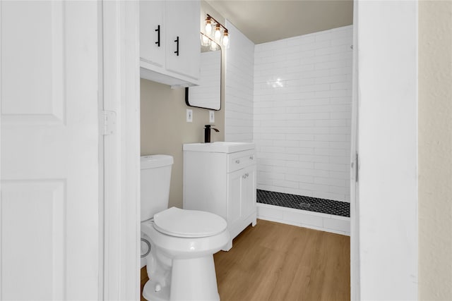 bathroom featuring tiled shower, hardwood / wood-style flooring, vanity, and toilet