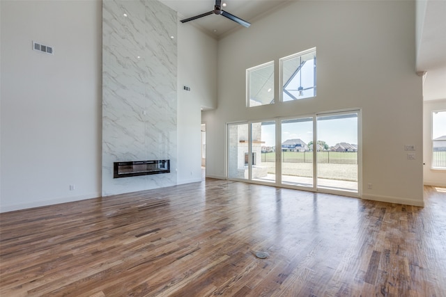 unfurnished living room with ceiling fan, a fireplace, hardwood / wood-style floors, and a high ceiling