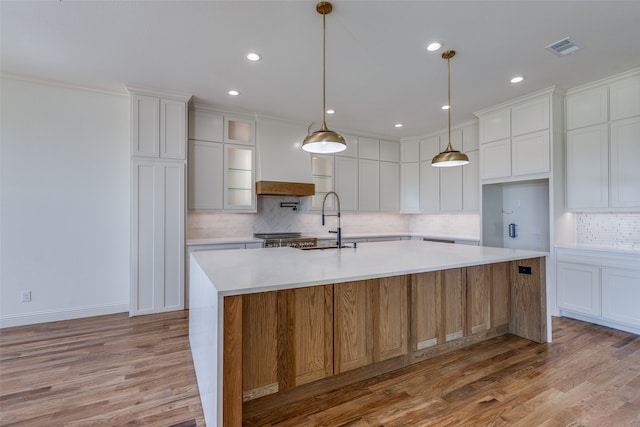 kitchen with white cabinets, light hardwood / wood-style floors, a large island with sink, and sink