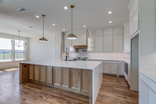 kitchen featuring pendant lighting, a kitchen island with sink, white cabinets, backsplash, and hardwood / wood-style floors