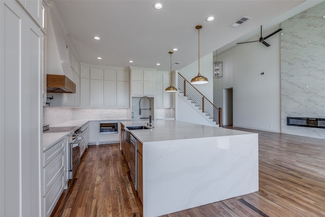 kitchen featuring wood-type flooring, electric range, a kitchen island with sink, white cabinets, and ceiling fan