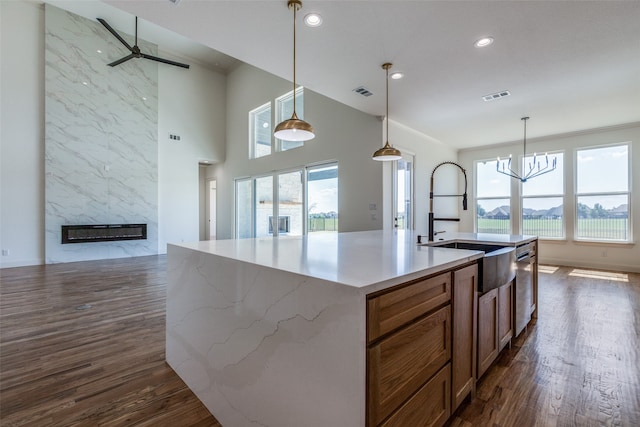 kitchen with a kitchen island with sink, ceiling fan with notable chandelier, hanging light fixtures, a fireplace, and dark hardwood / wood-style flooring