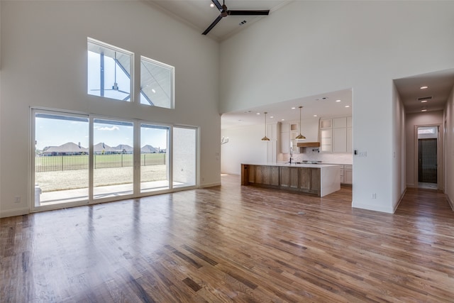 unfurnished living room with wood-type flooring, a towering ceiling, and ceiling fan