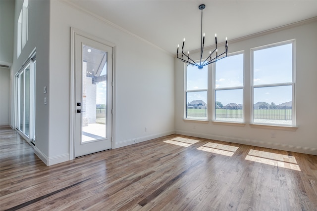 unfurnished dining area with an inviting chandelier, light wood-type flooring, a healthy amount of sunlight, and crown molding